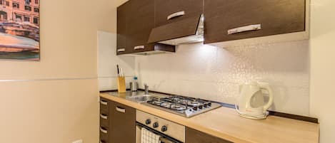Una cocina con armarios de madera oscura, una estufa a gas, una tetera y un lavamanos.