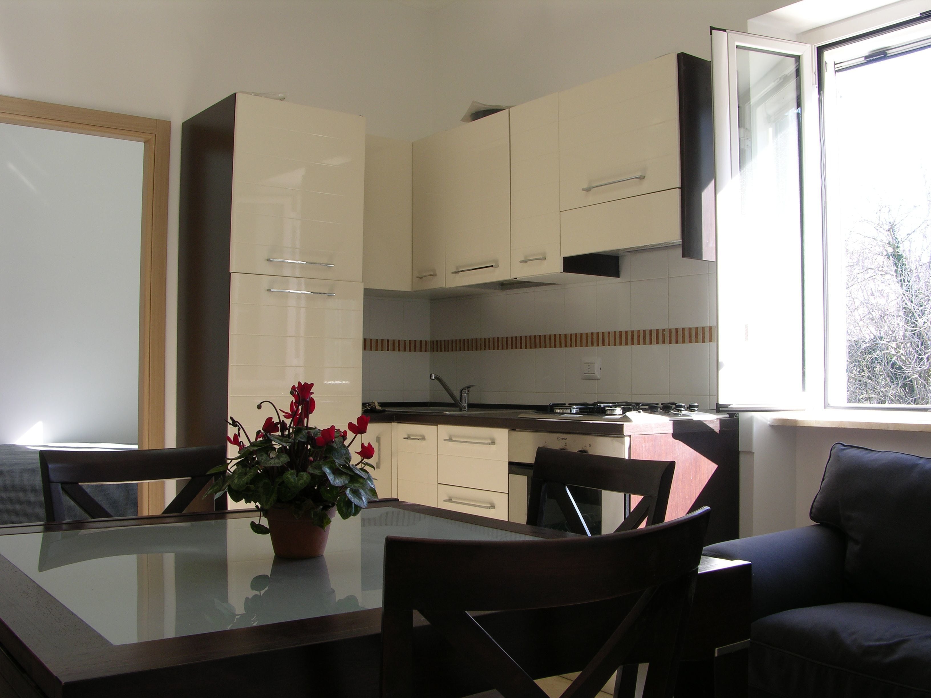 Una cocina moderna con armarios blancos, una mesa de comedor con sillas y una ventana que proporciona luz natural.