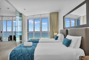 Habitación de hotel con dos camas, un ventanal con vistas al mar y un puerta de cristal que da a un balcón.