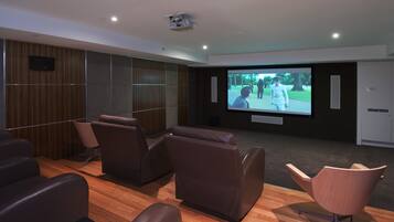 A modern home theater with leather recliners, a large flat-screen TV, and a wooden floor.