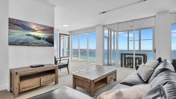 Un ampio soggiorno con una grande finestra vista mare, un tavolino in legno, un divano e una TV a parete.