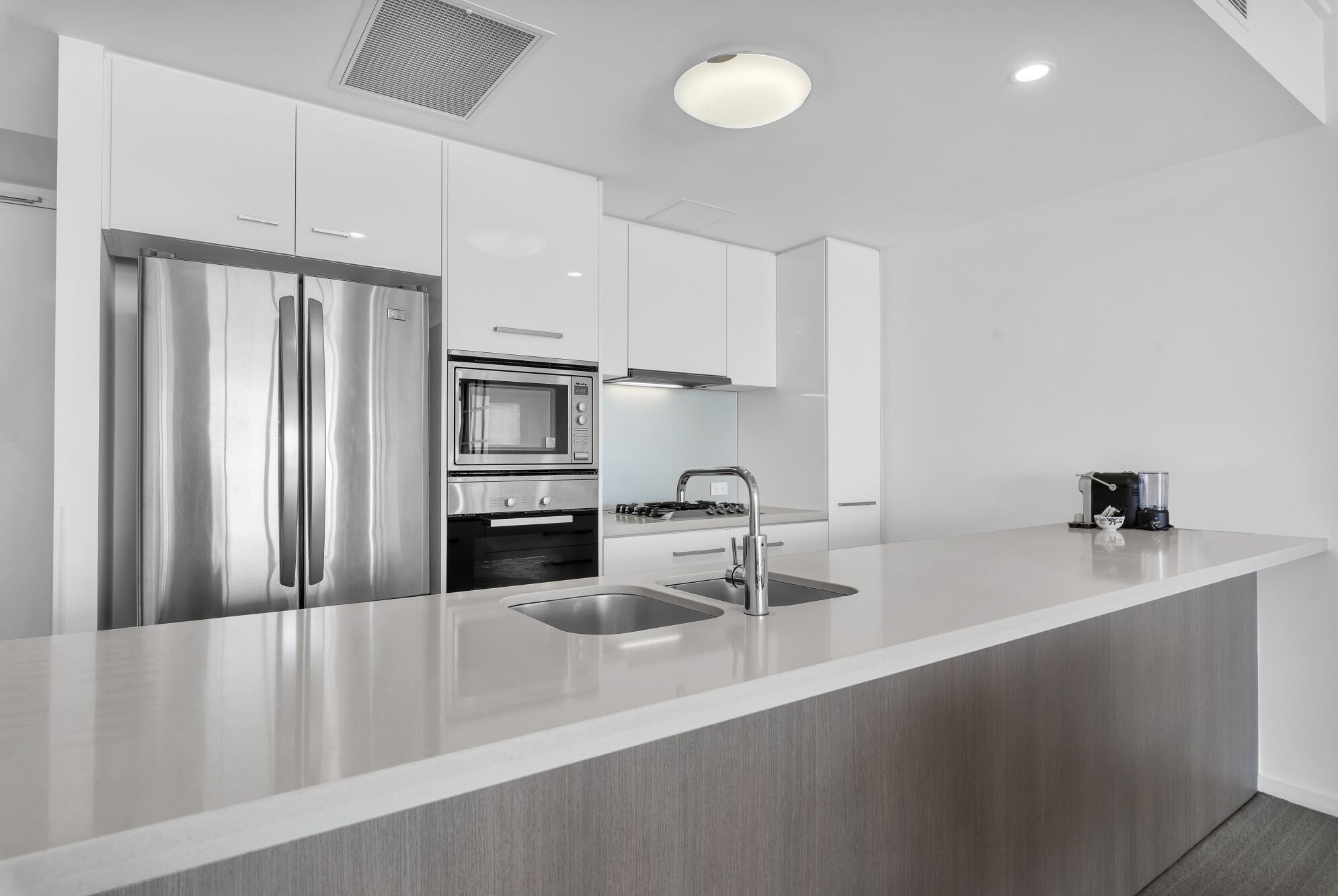 Une cuisine moderne dotée d’appareils électroménagers en acier inoxydable, d’un grand îlot central avec un évier et de meubles de rangement blancs.
