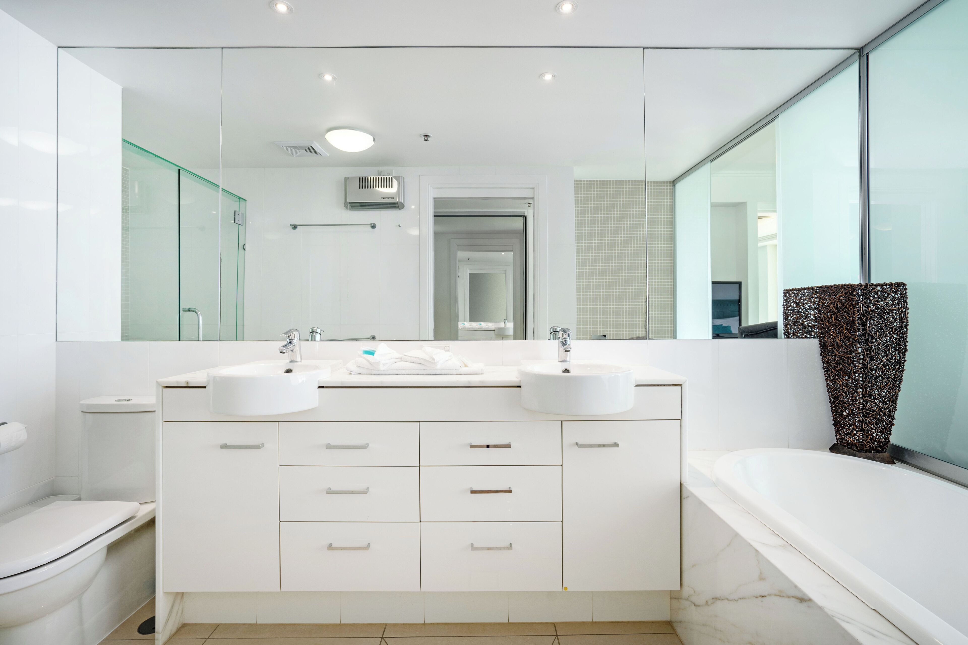 A modern bathroom with two sinks, a toilet, a bathtub, and a large mirror.
