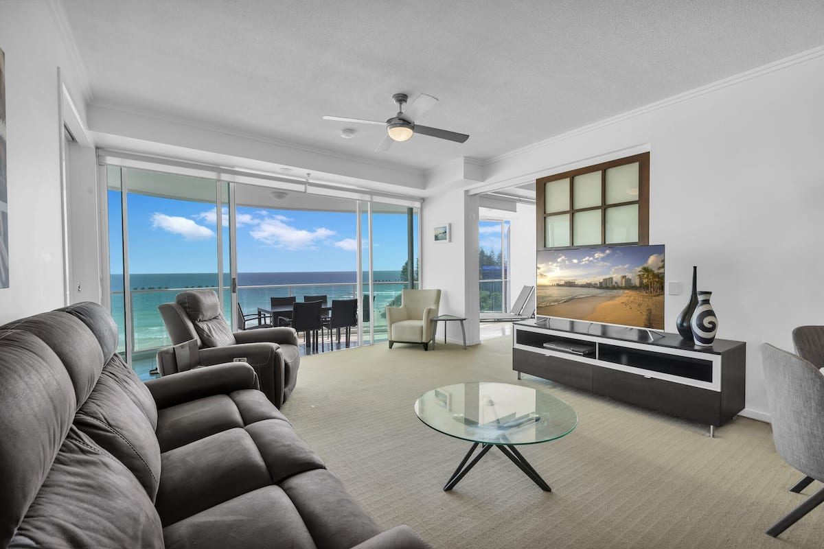 A modern living room with a large TV, comfortable seating, and a glass coffee table.