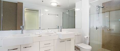 A modern bathroom with a large mirror, two sinks, a toilet, and a glass-enclosed shower.