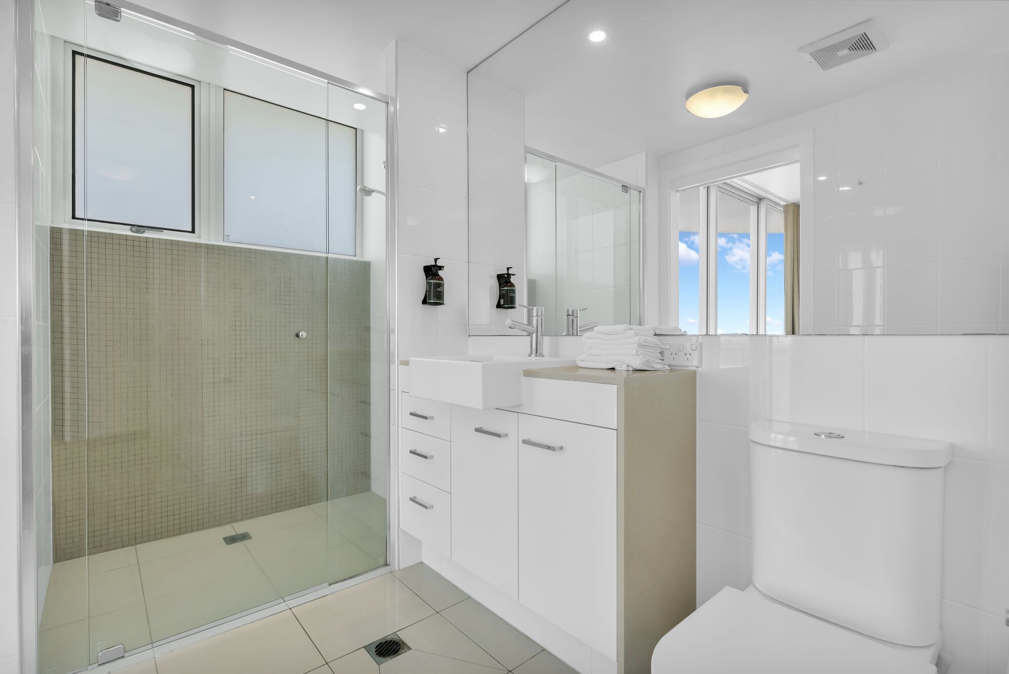 A modern bathroom with a glass-enclosed shower, white fixtures, and a view through the window.