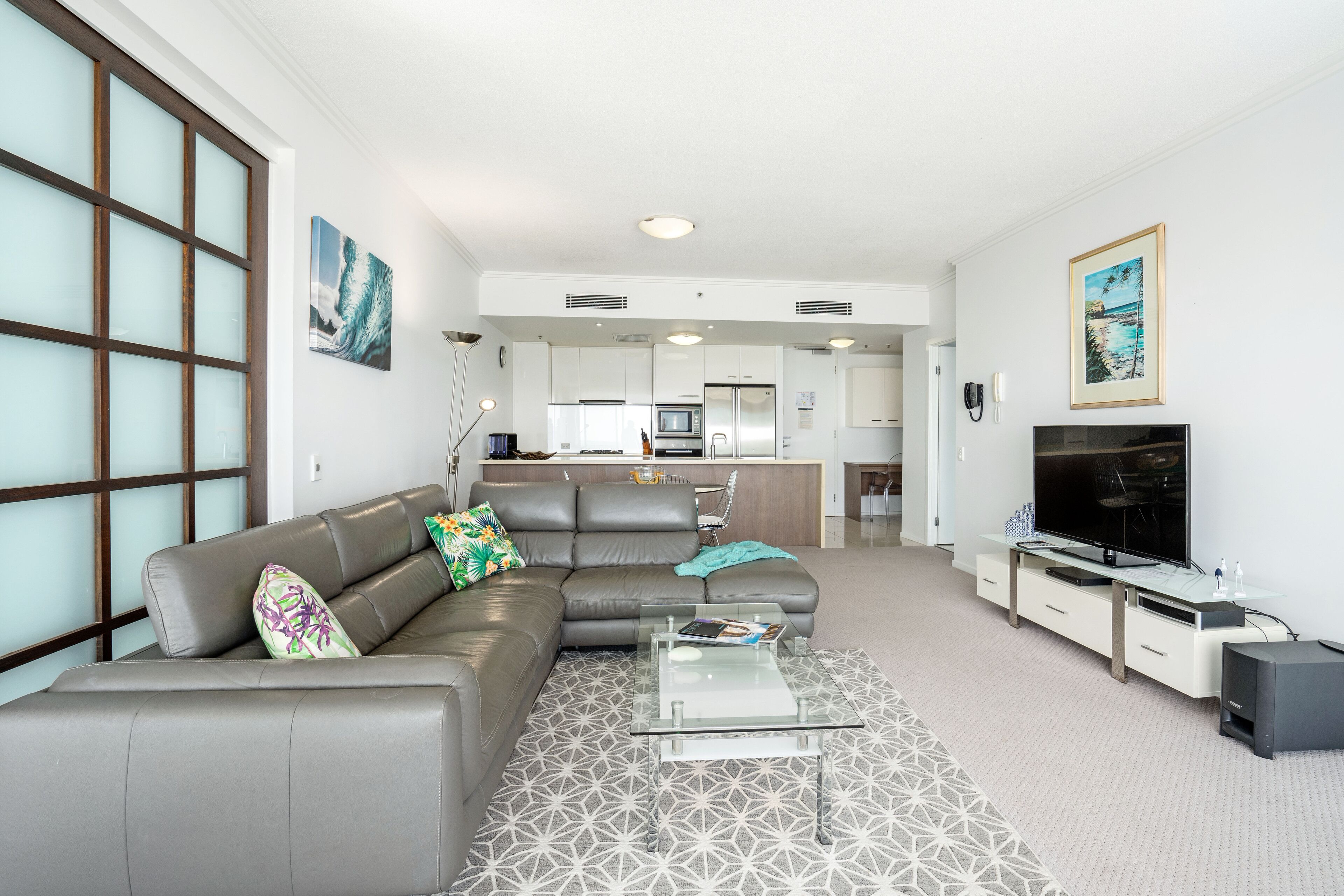 A modern living room with a grey sofa, a glass coffee table, and a flat-screen TV.