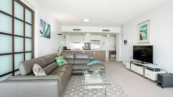 A modern living room with a grey sofa, a glass coffee table, and a flat-screen TV.