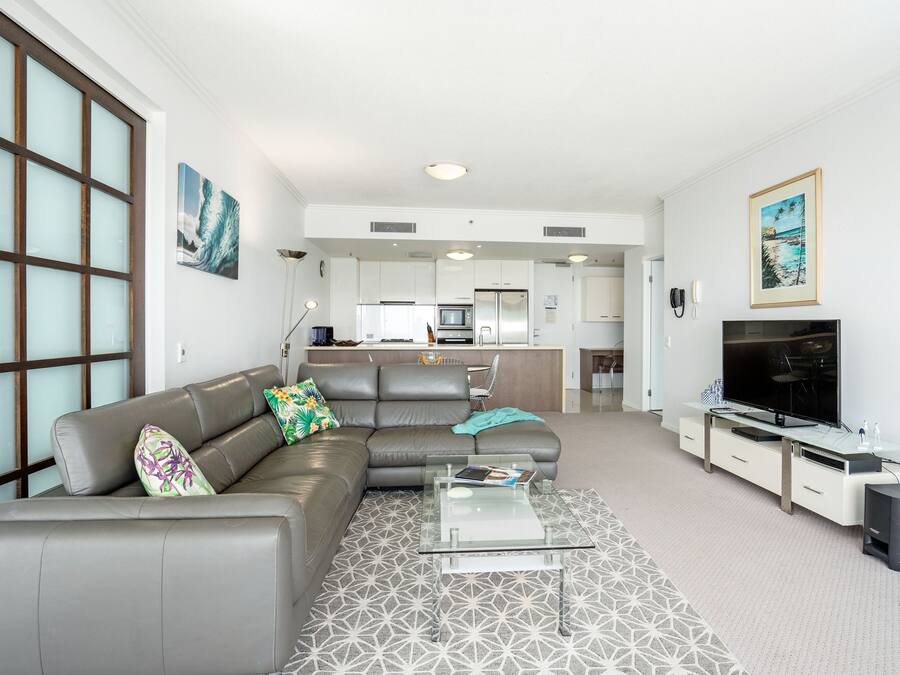 A modern living room with a grey sofa, a glass coffee table, and a flat-screen TV.