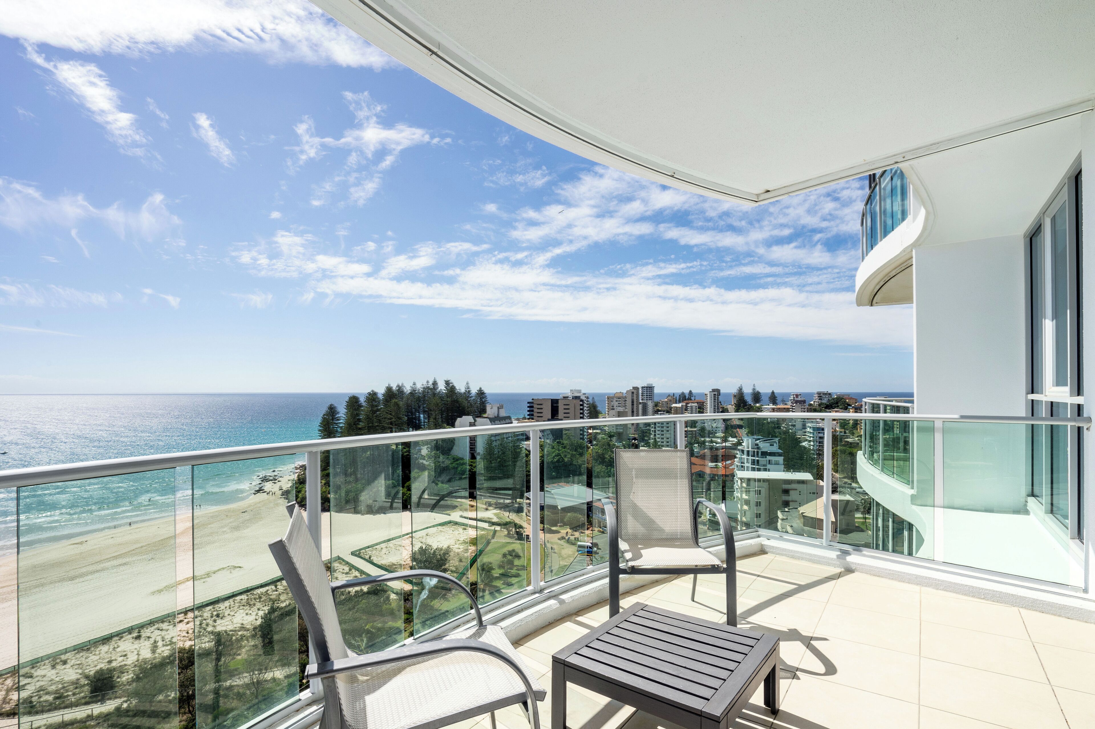 A balcony with a glass railing overlooking a beach and ocean.