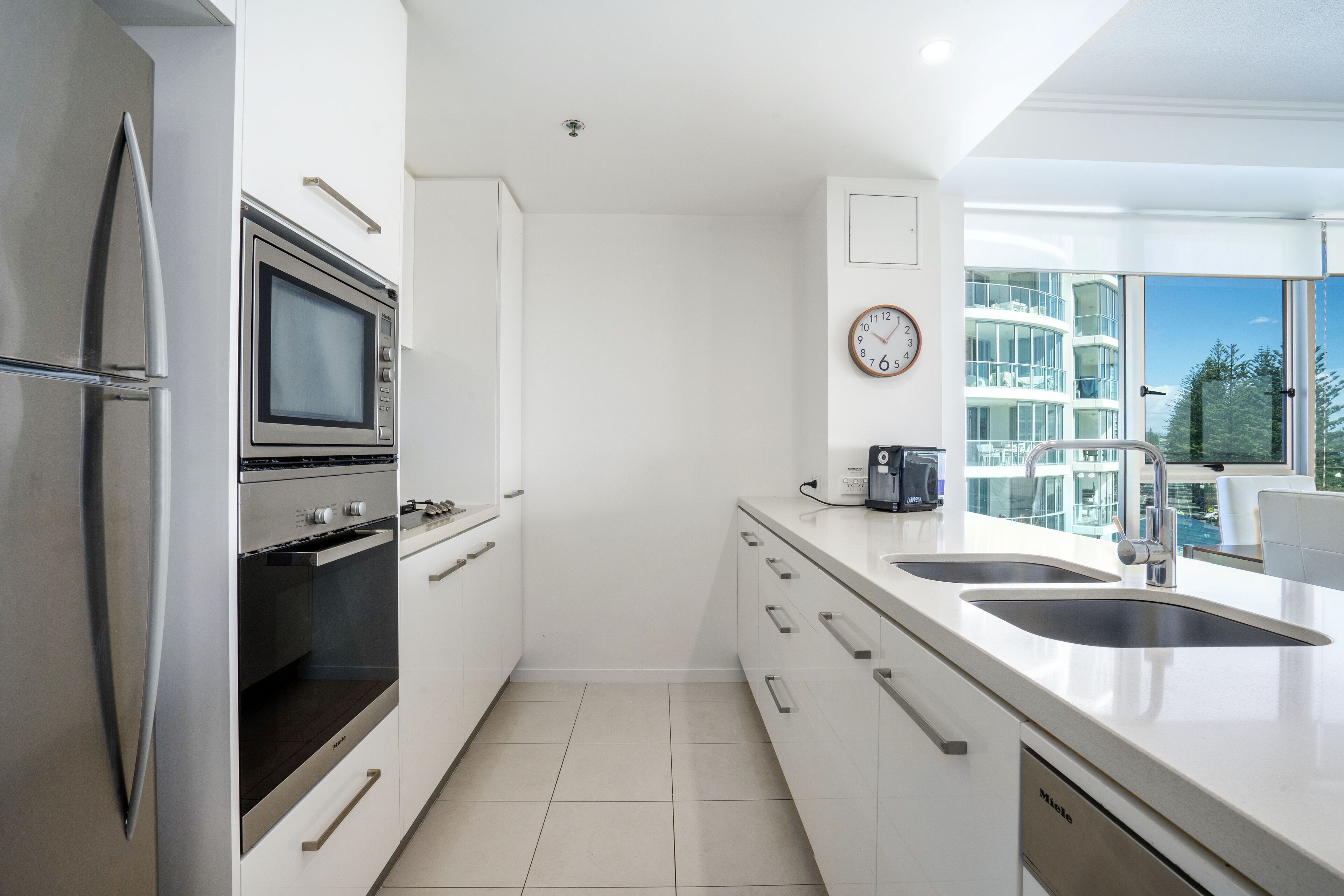 Una cocina moderna con electrodomésticos de acero inoxidable, un lavamanos doble y vistas a un edificio de gran altura.