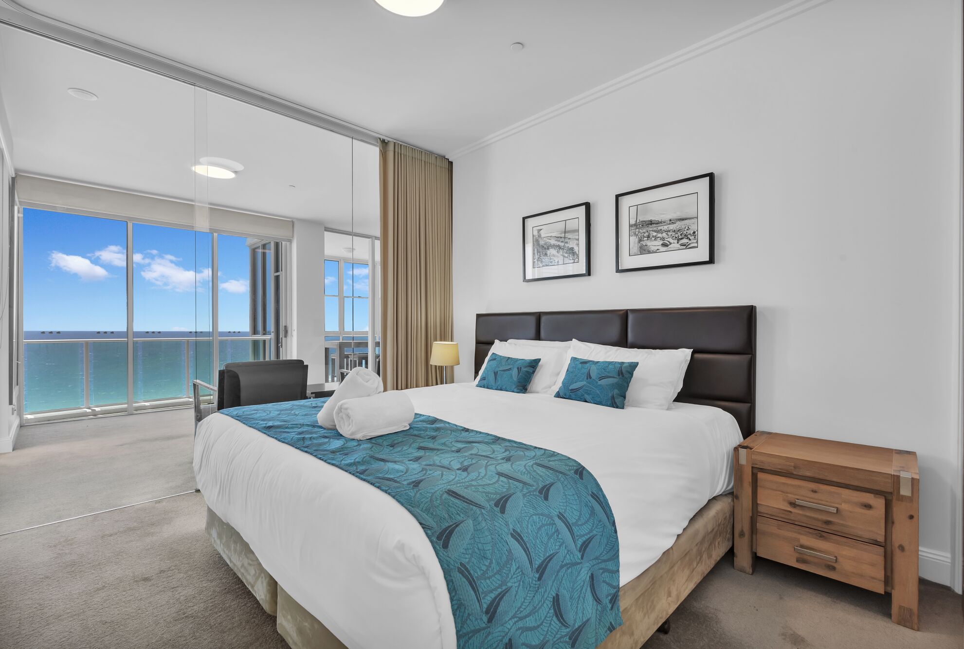 A hotel room with a large bed, a wooden nightstand, and a view of the ocean.