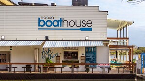Un restaurante frente al agua llamado 'Noosa Boathouse' con terraza y un letrero que dice 'Takeaway'.