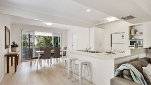Una cocina moderna con armarios blancos, una isla central con taburetes y una zona de comedor con mesa y sillas.