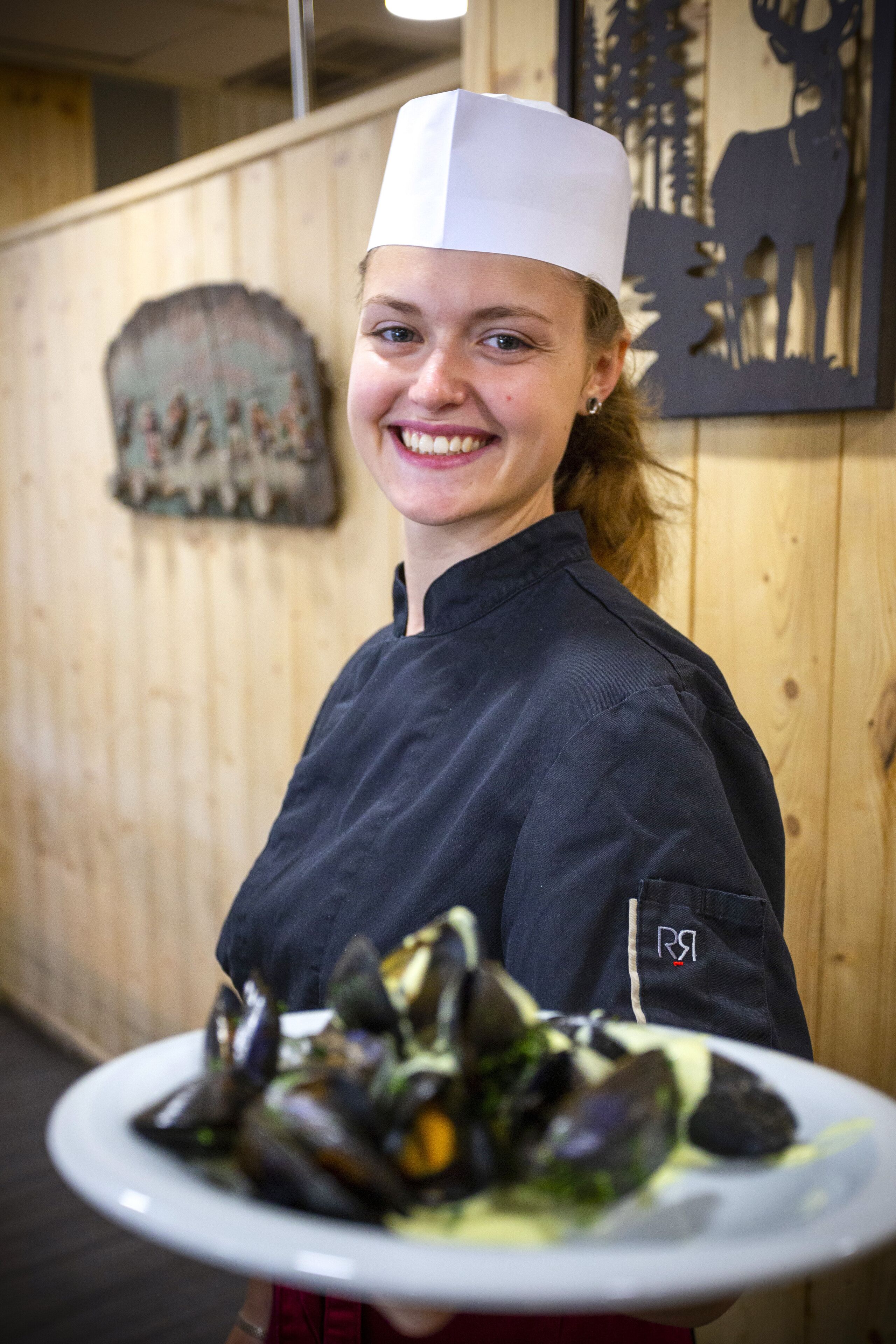 A person in a chef's uniform holding a plate of mussels.