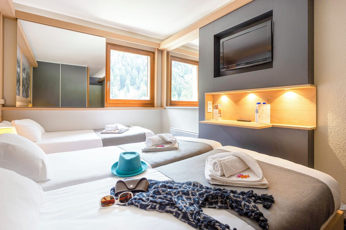Ein Hotelzimmer mit zwei Betten, einem an der Wand befestigten Fernseher und einer Ablage mit Annehmlichkeiten.