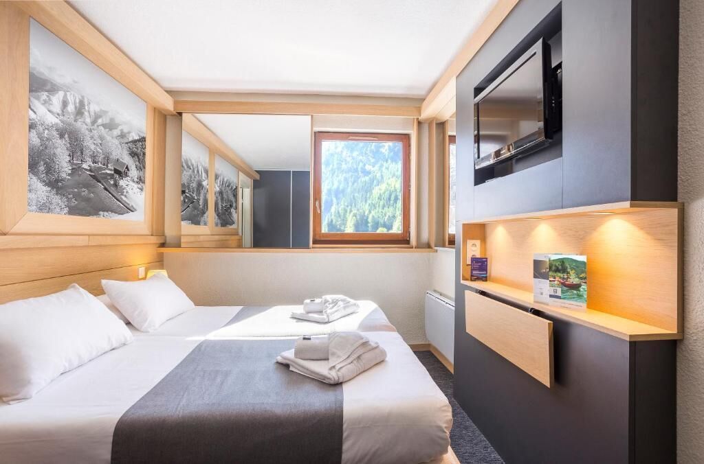 Une chambre d’hôtel équipée d’un lit, d’un bureau, d’une télévision et d’une fenêtre donnant sur des arbres.