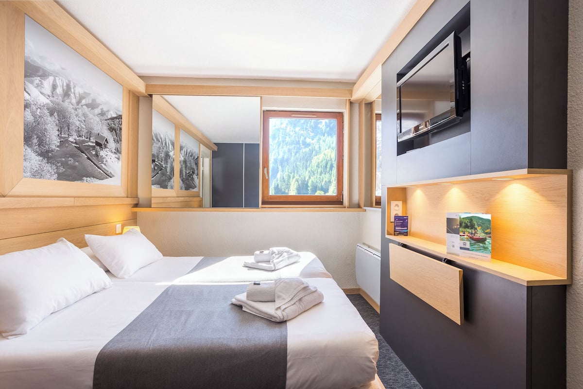 Ein Hotelzimmer mit zwei Betten, einem großen Fenster, einem Flachbildfernseher und einem Holztisch mit Lampe.