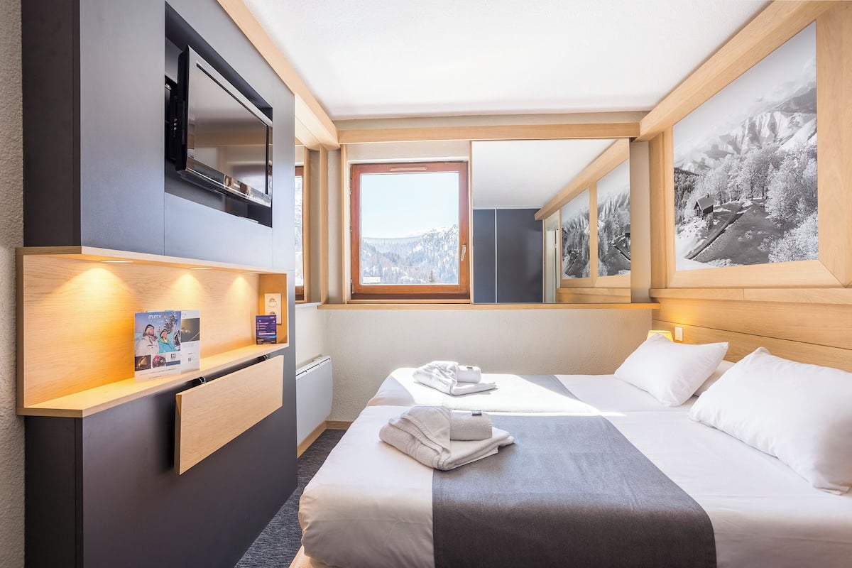 Ein Hotelzimmer mit Bett, Schreibtisch, Fernseher, Fenster mit Bergblick und einem gerahmten Bild an der Wand.