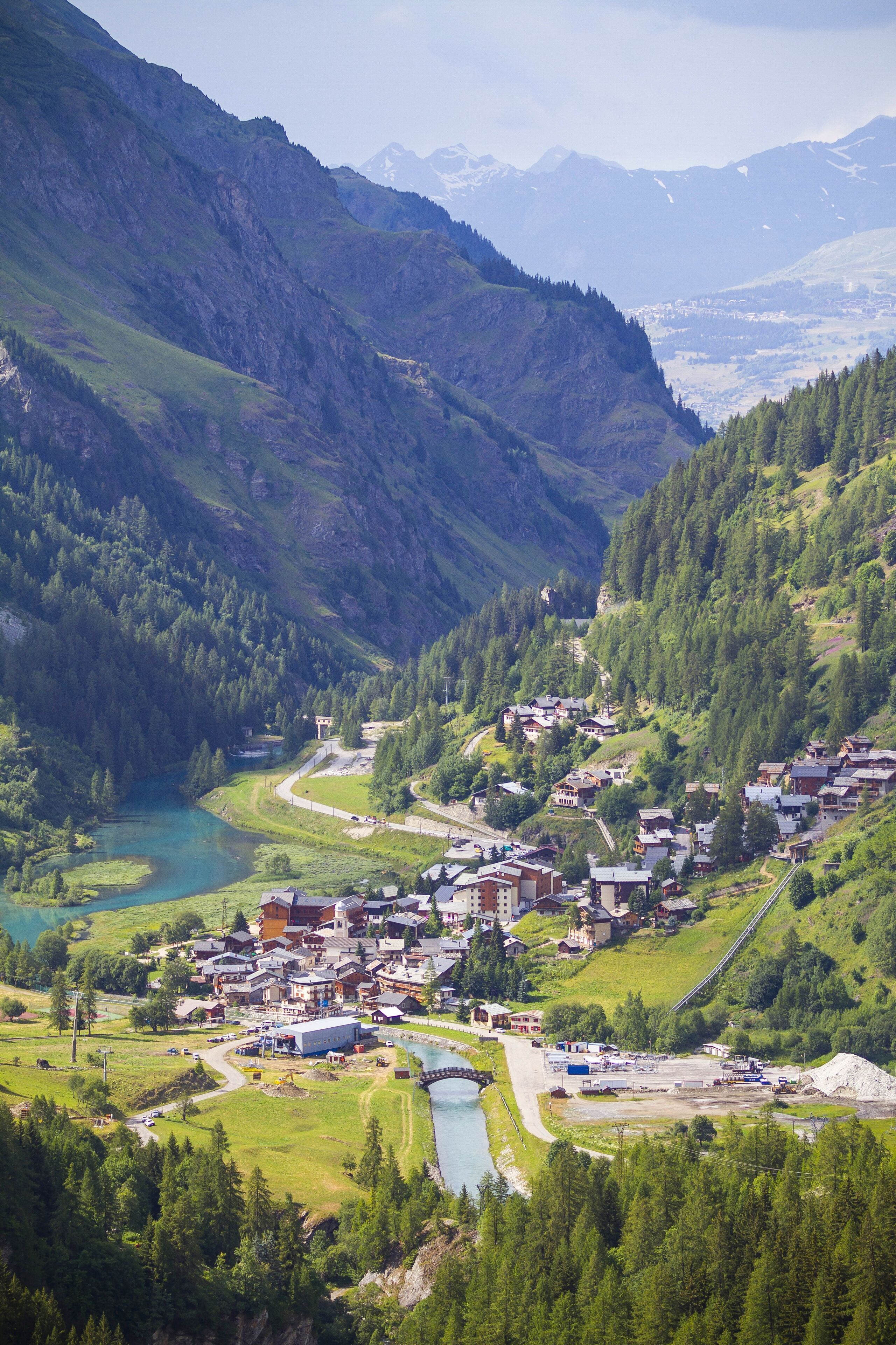 Un village de montagne avec une rivière, des maisons et un pont.