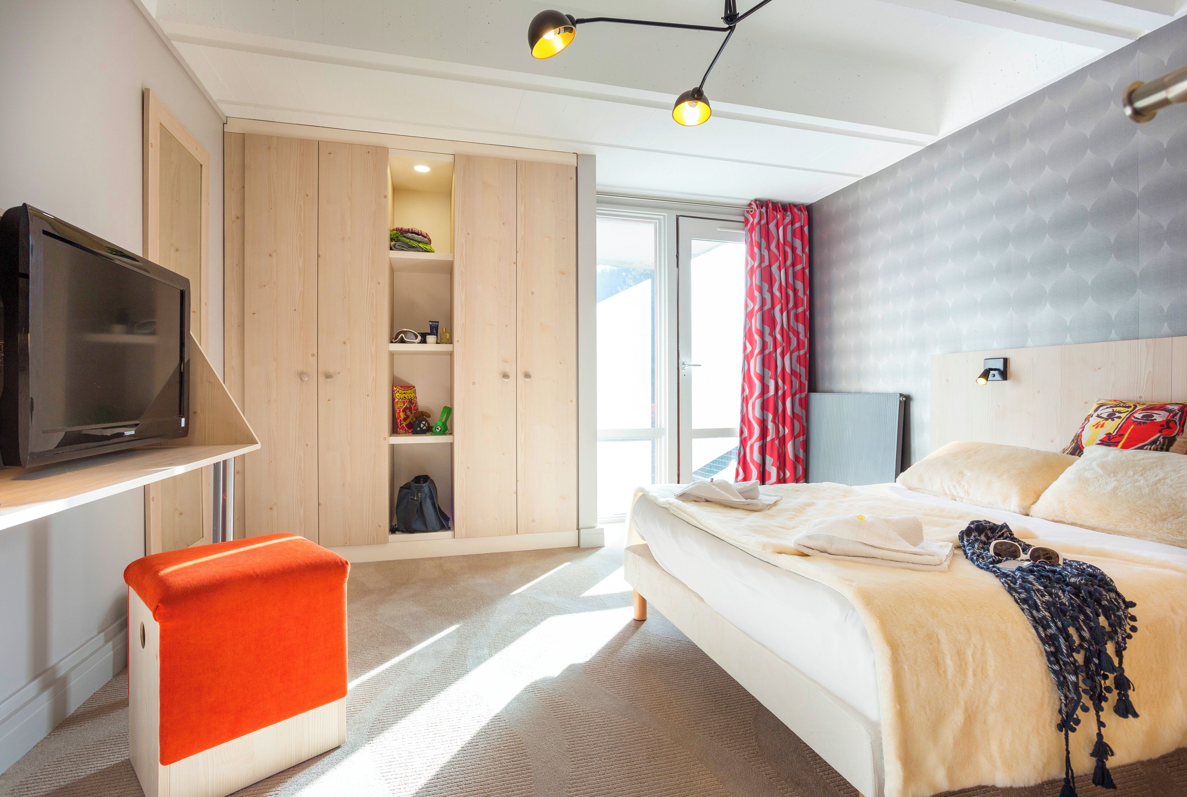 Une chambre à coucher avec un lit, une télévision, une armoire et une fenêtre avec des rideaux.
