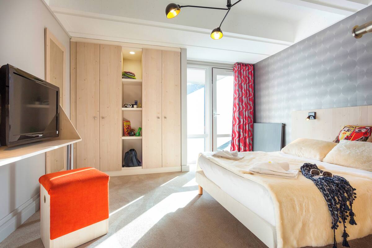 Een slaapkamer met een bed, een televisie, een kledingkast en een raam met gordijnen.