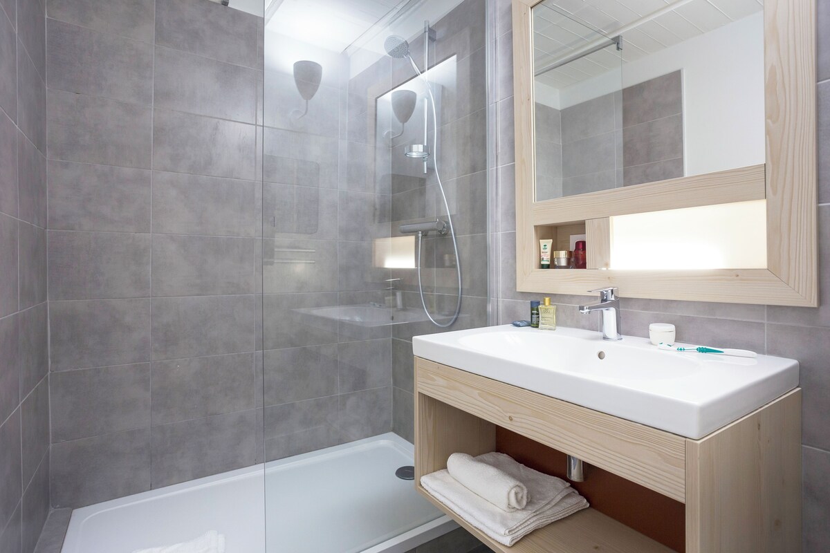 Een moderne badkamer met een douchecabine van glas, een witte wastafel en een houten wastafelmeubel.