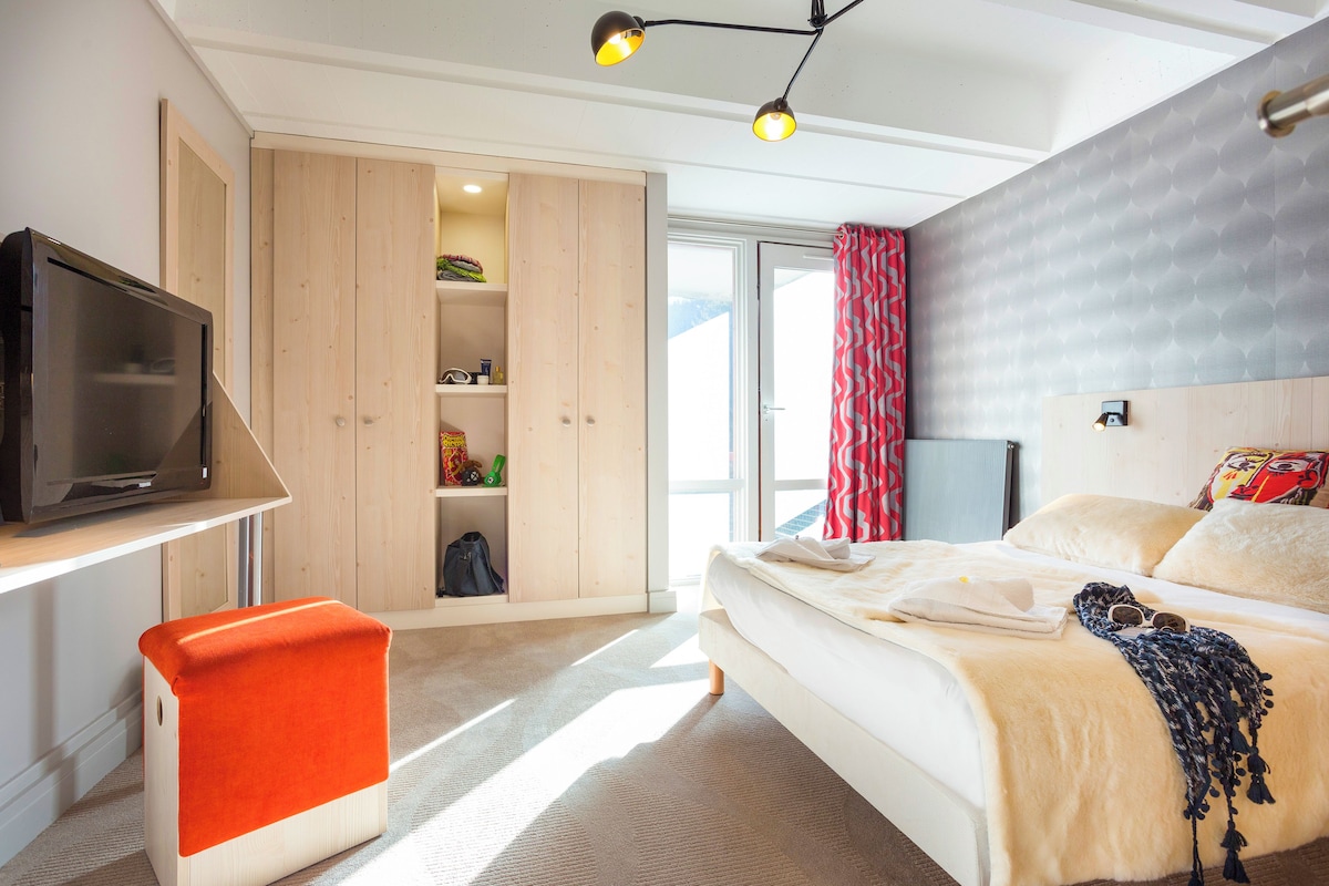 Een slaapkamer met een bed, een televisie, een kledingkast en een raam met gordijnen.