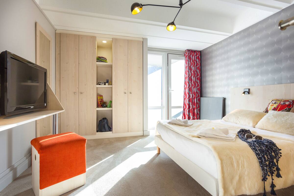 Een slaapkamer met een bed, een televisie, een kledingkast en een raam met gordijnen.