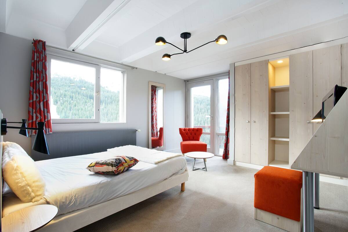 Een moderne slaapkamer met een bed, een rode stoel, een kleine tafel en een trap naar een vide.