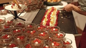 Un chef prépare des desserts dans une cuisine. On peut voir sur un plateau un long dessert au chocolat et, à côté, de petits ramequins remplis de fruits rouges.