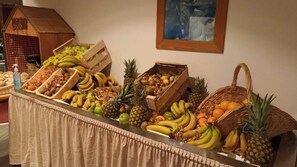 Een buffettafel met verschillende soorten fruit en groenten, zoals bananen, ananassen en sinaasappels.