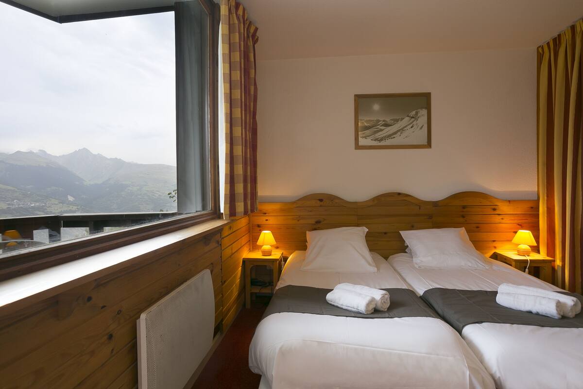 Een kamer met twee bedden, een raam met uitzicht op bergen, houten wanden en twee bedlampjes.
