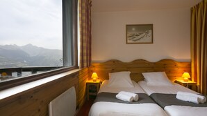 Une chambre avec deux lits, une fenêtre donnant sur la montagne, des murs en bois et deux lampes de chevet.