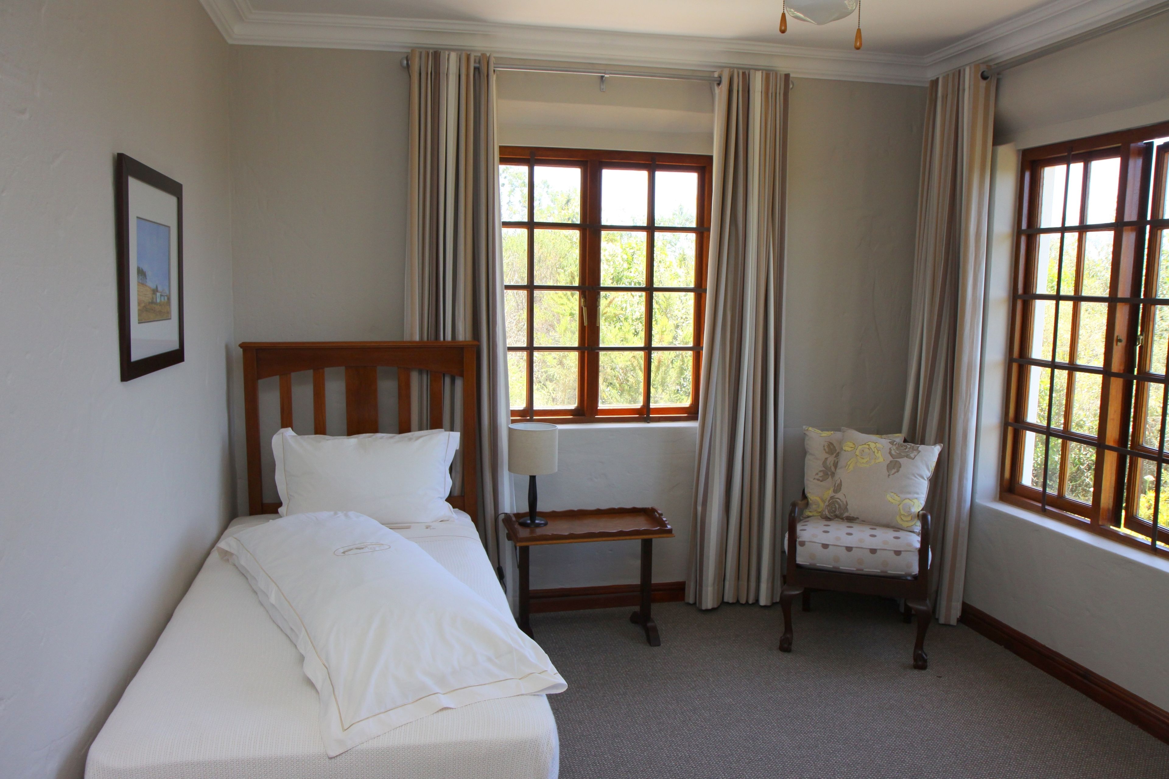 A room with a bed, a chair, a small table, and a window with curtains.