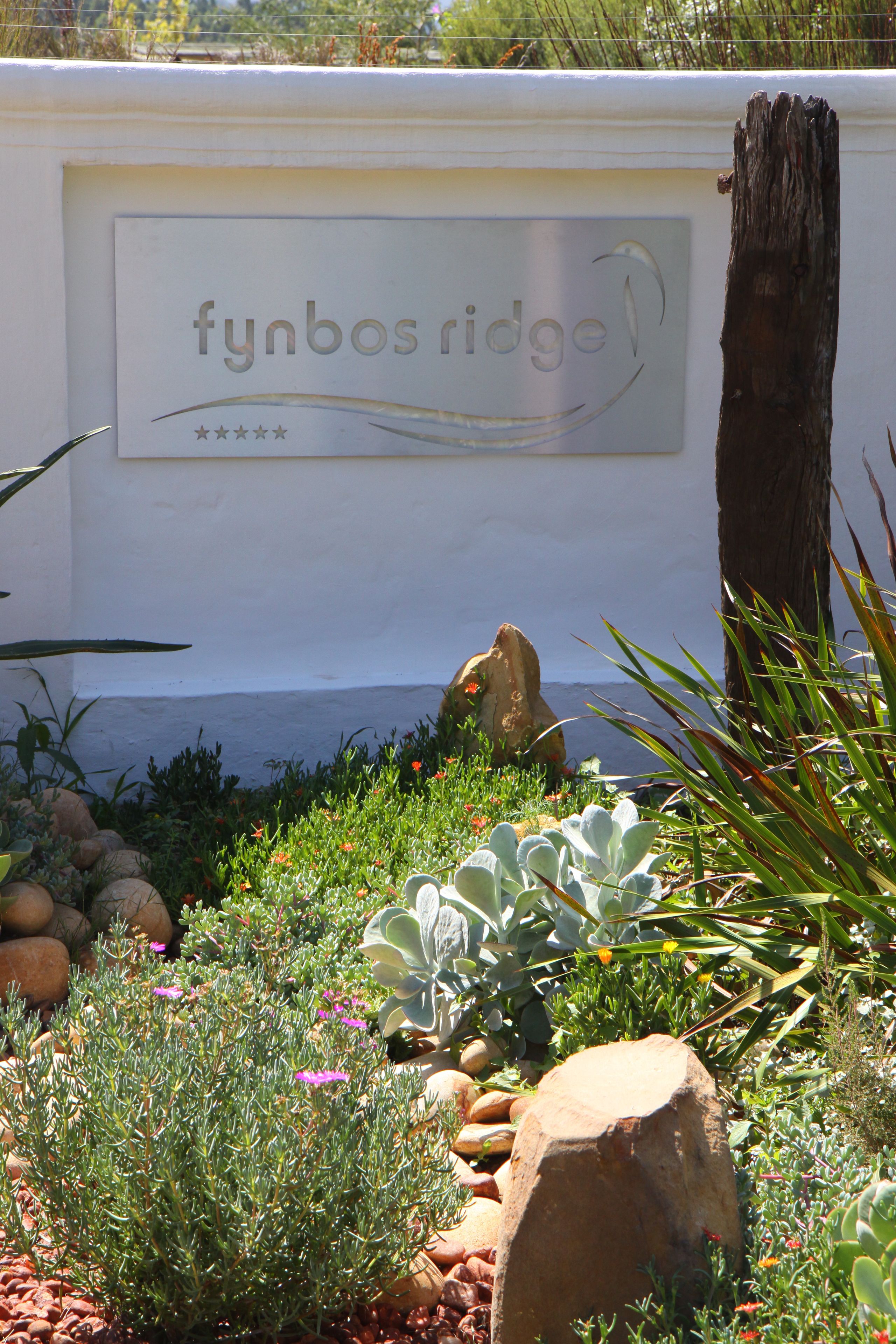 A garden with a sign that reads "fynbos ridge" and a large tree trunk.