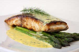 A plate with a piece of fish, asparagus, and a creamy sauce.