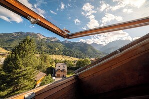 A view from a wooden balcony overlooking a mountainous landscape with a small house and a church. - VVF Serre Chevalier Briançon (Monetier-les-Bains)