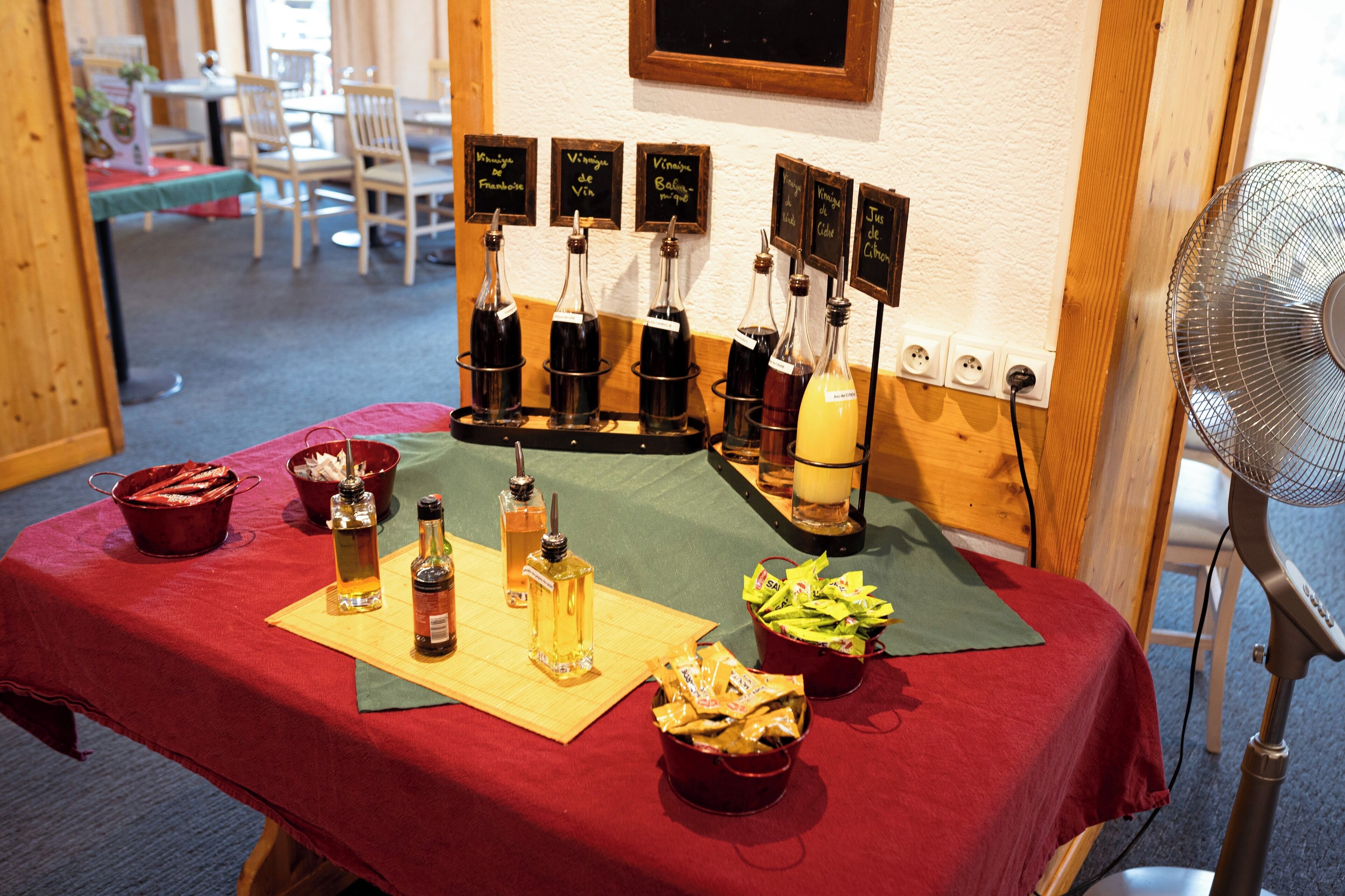 Een tafel met flessen wijn en snacks, een ventilator en een krijtbordmenu.