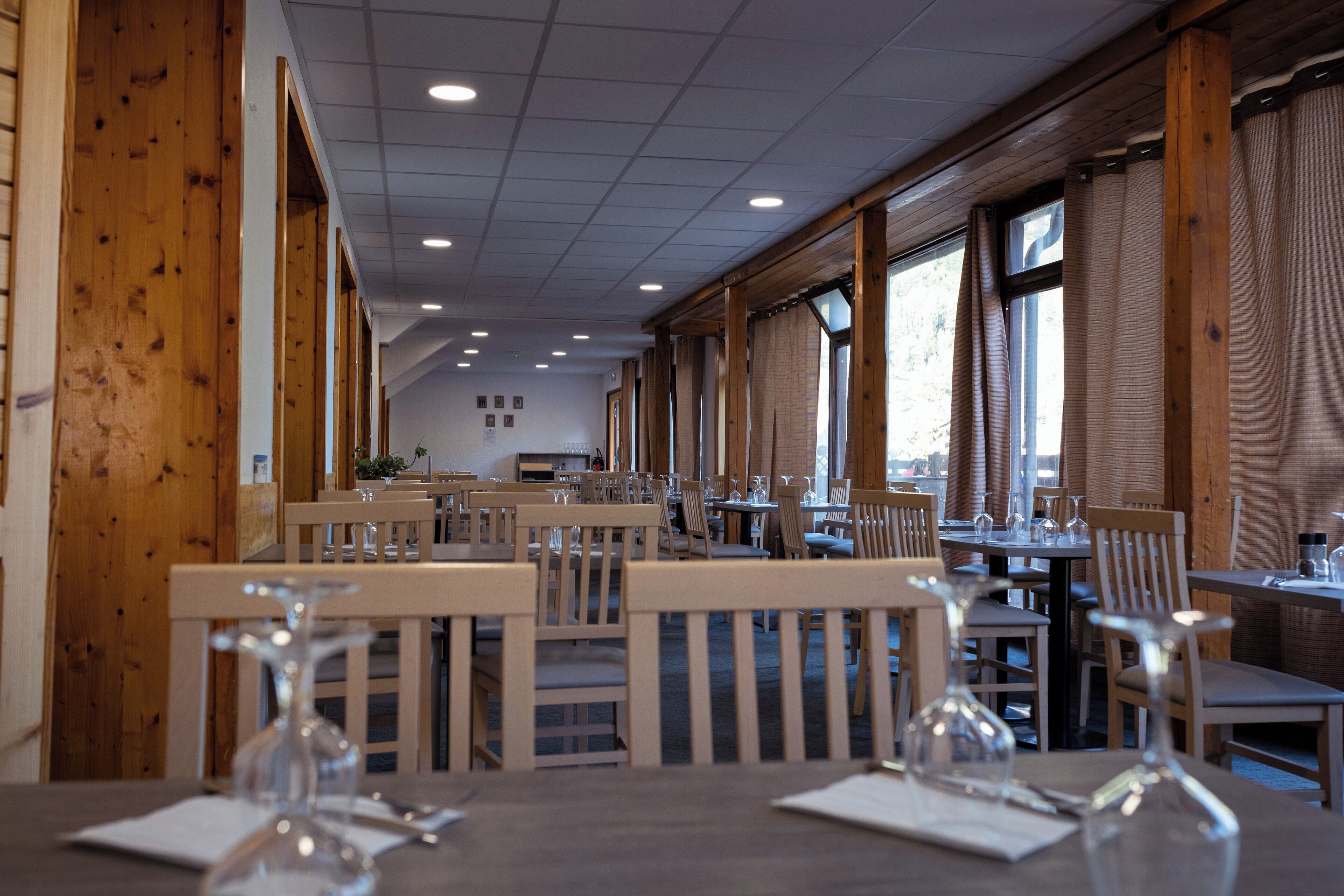 A restaurant with wooden walls and ceiling, multiple tables with chairs, and large windows.