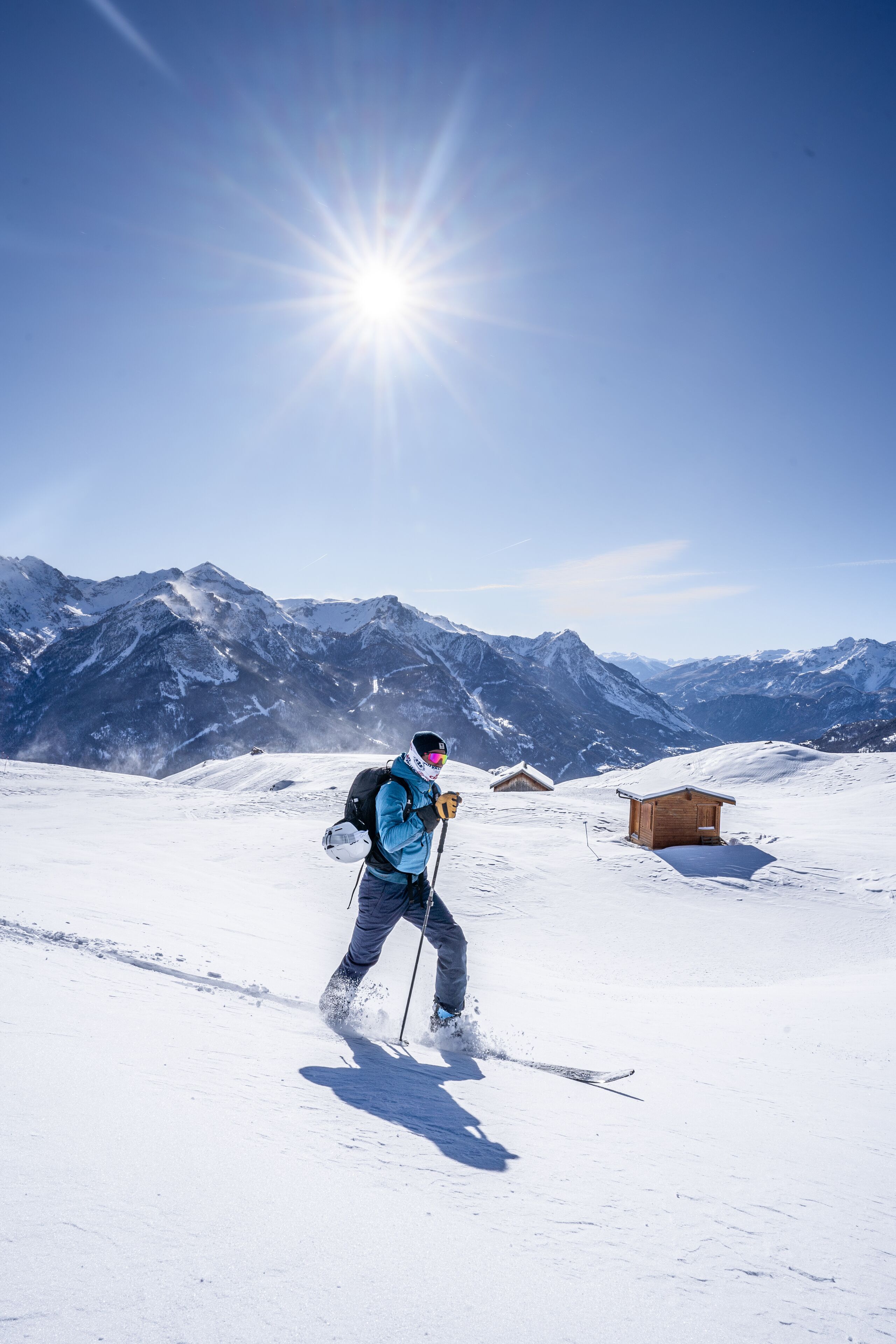 A person skiing on a snowy mountain with a clear sky and a wooden cabin in the background.