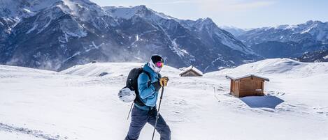 A person skiing on a snowy mountain with a clear sky and a wooden cabin in the background.