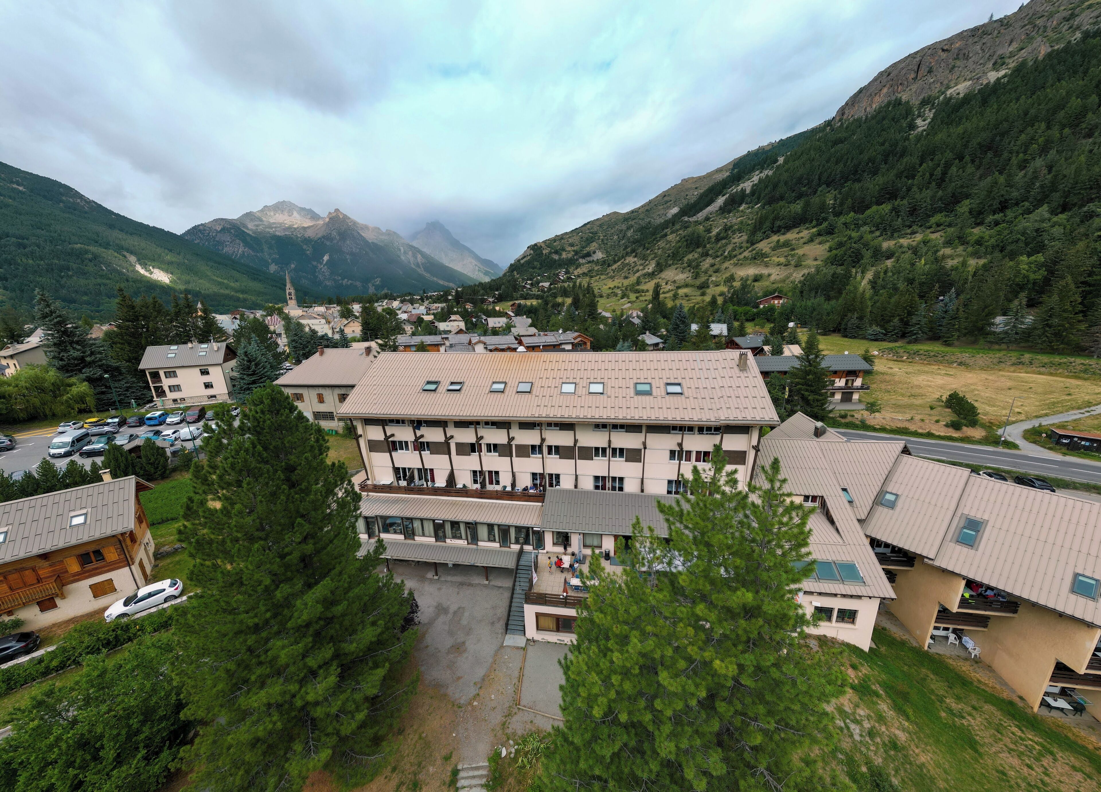 Ein mehrstöckiges Hotel mit flachem Dach, umgeben von Grünflächen und Bergen.