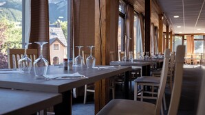 Un restaurante con largas mesas dispuestas para comer, amplias ventanas que ofrecen vistas a la montaña y vigas de madera en el techo.