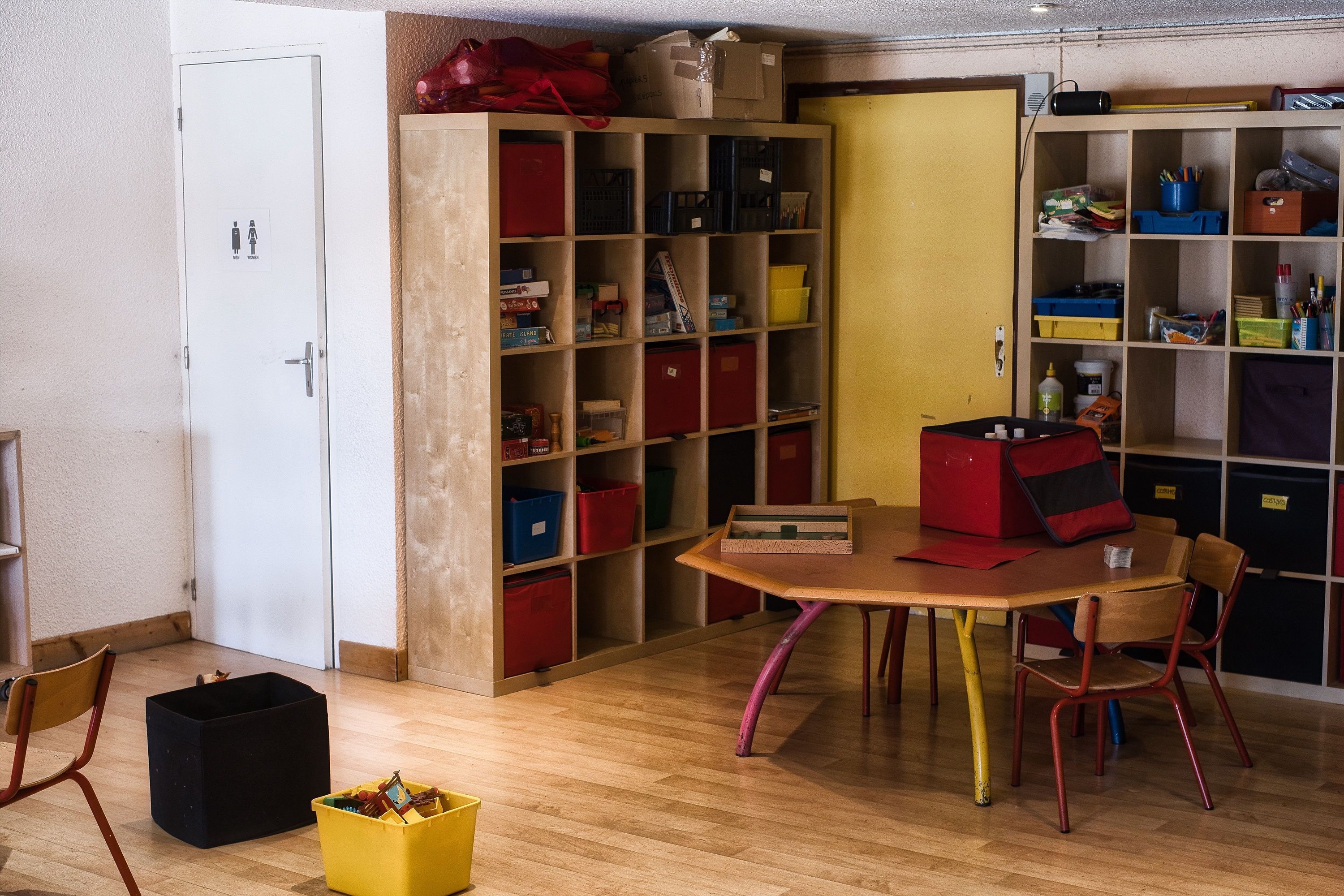 A room with a wooden table, chairs, and a bookshelf filled with storage boxes.