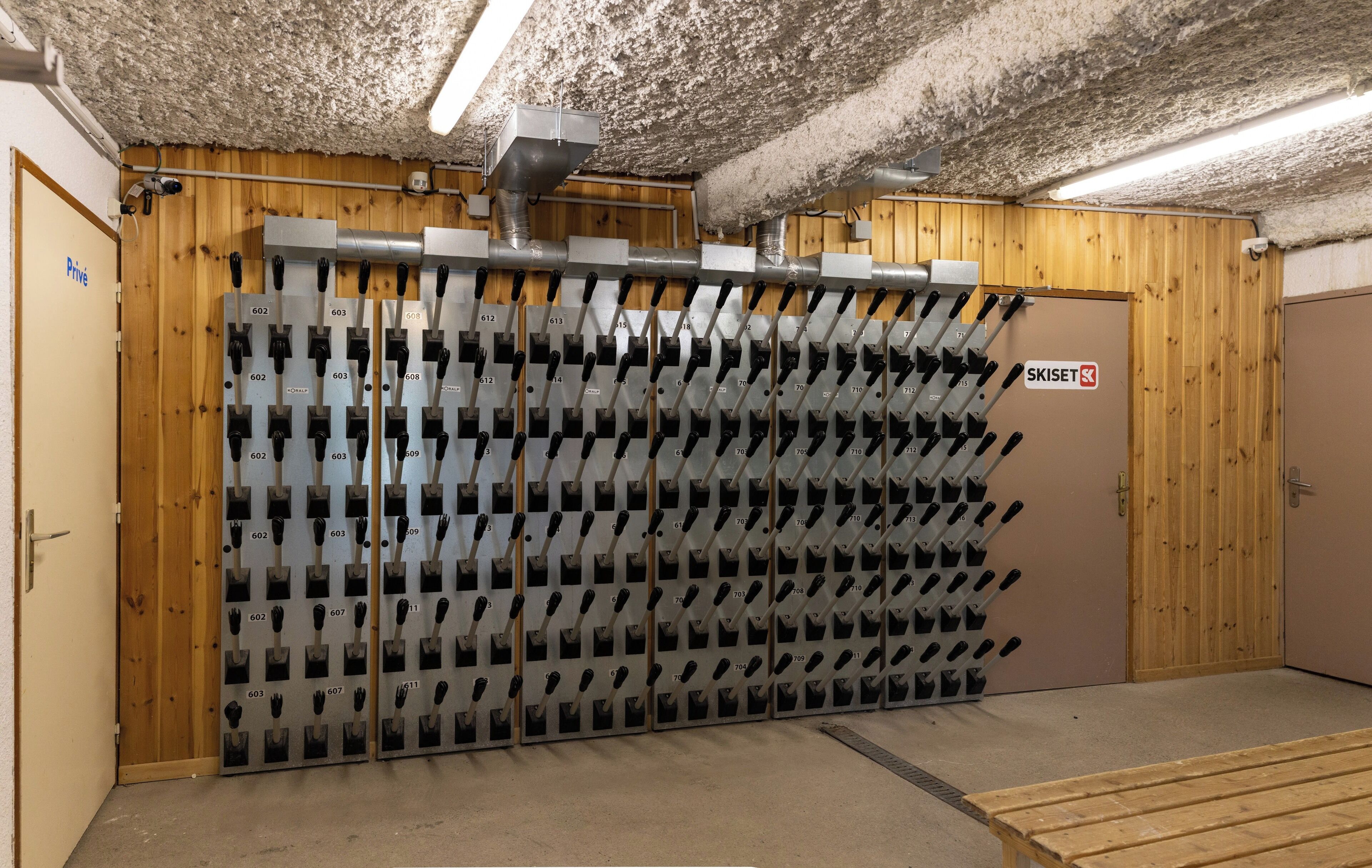 A ski storage room with rows of skis and ski boots, a wooden door, and a sign indicating 'SKISSET'.