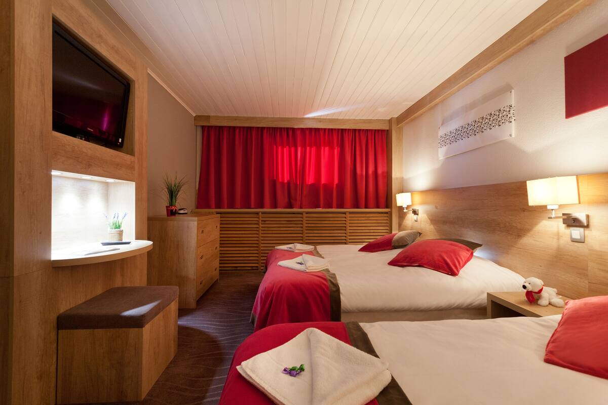 A hotel room with two beds, a TV, a desk, and a red curtain.