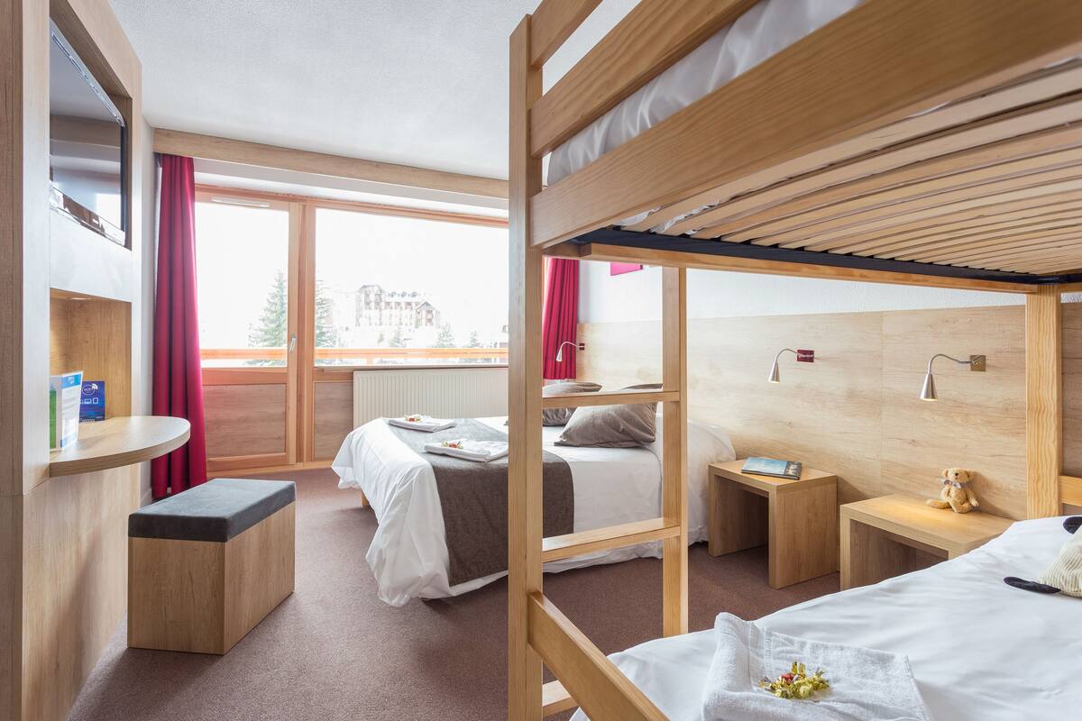 A hotel room with bunk beds, a desk, a chair, and a window with curtains.