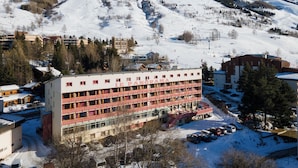Un hotel de fachada roja, con varios pisos y una pista de esquí al fondo.