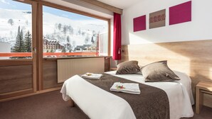 Habitación de hotel con un ventanal grande, cabecera de madera, dos camas y vista a una montaña nevada.